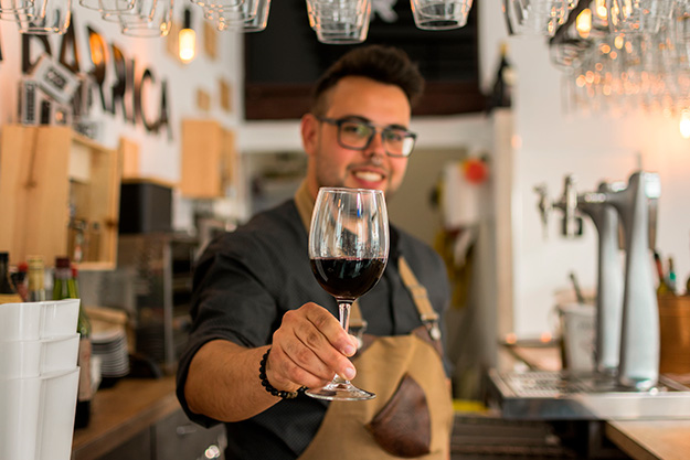 Sommelier chileno ofreciendo una copa de vino tinto en un restaurante moderno, representando el servicio de vinos profesional.
