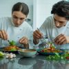 Dos chefs profesionales emplatando con pinzas fideos y vegetales frescos, representando un curso de cocina asiática de Indonesia y Vietnam.