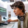 Joven editor trabajando en edición de audio en computador con software de mezcla, micrófono y audífonos en un estudio de producción sonora.