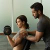 Entrenador guiando ejercicio de tonificación muscular con mancuernas en gimnasio, enfocándose en técnica y control del movimiento.