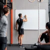 Grupo de personas en un gimnasio planificando proyectos deportivos en una pizarra blanca.