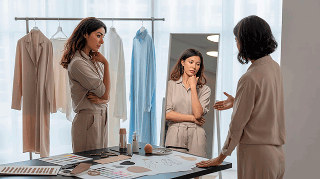 Mujer analizando su estilo personal frente al espejo con asesoría de imagen y prendas en tonos neutros en un entorno luminoso
