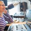 Mujer con audífonos grabando voz en estudio de audio profesional frente a micrófono y consola de sonido para locución comercial.