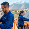 Instalador eléctrico clase d e instaladora de paneles fotovoltaicos chilenos realizando labores de instalación de paneles solares y tableros eléctricos en un barrio urbano con montañas de fondo.