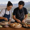Dos personas adultas preparan platos de cocina tradicional chilena con recetas típicas del norte, centro e insular y sur de Chile en una cocina rústica.